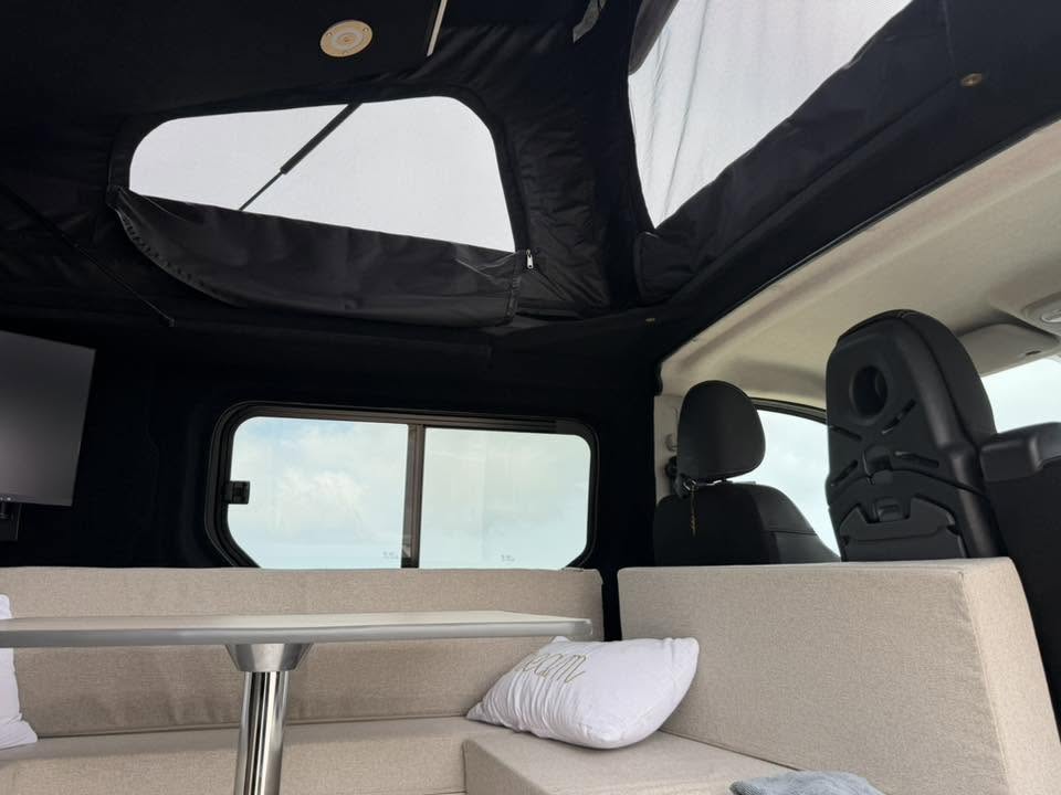 Intérieur aménagé d'un van avec toit relevable ouvert, banquette et table